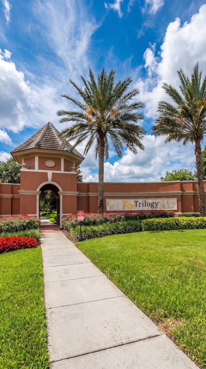 Stucco entrance gate and sign with palm trees for Trilogy Orlando, a 55-plus resort community in Groveland, FL.